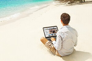 Фото человека, сидящего на пляже с ноутбуком, удаленная работа